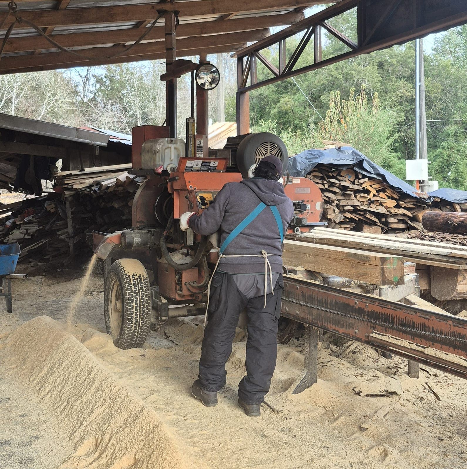 Trabajador de Aserradero El Arenal operando una máquina aserradora, rodeado de aserrín y madera apilada